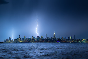 Wall Mural - Lightning striking New York City skyscrapers at night. Stormy skies over Midtown West Manhattan from the Hudson River