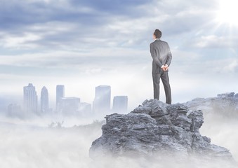 Wall Mural - Business man standing on rock looking at misty skyline