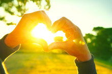 Person Making Heart With Hands Over Nature Sunset Background. Silhouette Hands In Heart Shape With Sun Inside