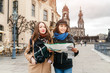 © EdNurg - Two charming cheerful women are walking with a map along Dresden Street, Germany. The concept of love and friendship in travel