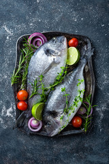 Fresh uncooked Dorado fish or sea bream with ingredients for cooking on dark background, top view