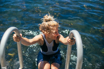 Wall Mural - female blonde cute skinny cyclist makes a break from super hot summer bicycle ride to swim in a bright blue lake with bikes laying on dock.