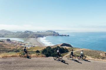 Wall Mural - Group of cyclists, teammates, friends, descending windy narrow road next to the bay with fog and water and blue skys san francisco in norhtern california.