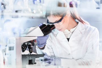 Poster - Life scientists researching in laboratory. Attractive female young scientist microscoping in their working environment. Healthcare and biotechnology.