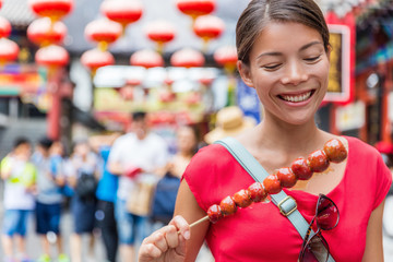 Wall Mural - Chinese woman eating Bing Tang Hulu, a traditional chinese food snack from Beijing. Fruit candy stick sold in outdoor market place on Wangfujing street. Candied fruits on a bamboo stick.