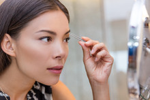 Asian Woman Plucking Eyebrows With Tweezers Using Eyebrow Tweezer At Home In Bathroom Makeup Mirror. Closeup Of A Girl's Face While She Is Removing Her Facial Hairs. Eyebrows Beauty Care.