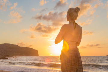 Silhouette of young woman practicing yoga on sandy beach at sunset.