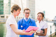 © Myroslava - Happy young doctor and nurses look at folder during coffee break, outdoors