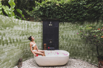 Wall Mural - Woman relaxing in round outdoor bath with tropical flowers, organic skin care, luxury spa hotel, lifestyle photo