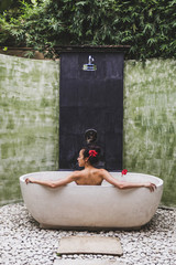 Wall Mural - Woman relaxing in round outdoor bath with tropical flowers, organic skin care, luxury spa hotel, lifestyle photo