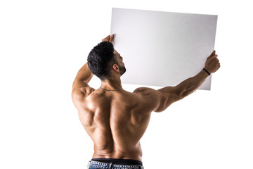 Naked young male bodybuilder holding blank white sign, isolated on white background, seen from the back, large copyspace