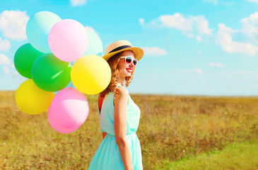 Happy smiling woman with an air colorful balloons enjoying a summer day on a meadow blue sky