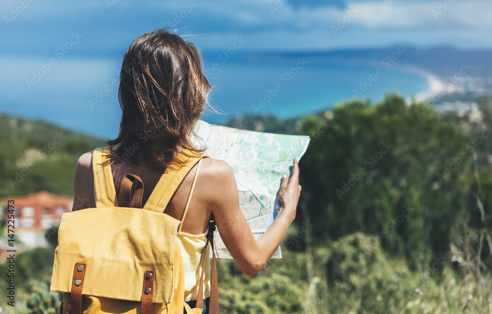 Hipster tourist hold and look map on trip, lifestyle concept adventure, traveler with backpack on background mountain and blue sea landscape horizon, young girl hiker pointing hands on trekking plan - obrazy, fototapety, plakaty 