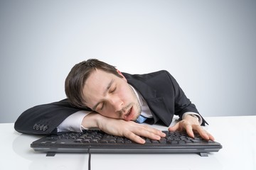 Tired or exhausted overworked businessman is sleeping on keyboard.