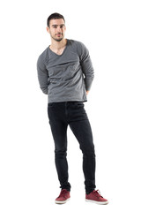 Wall Mural - Young handsome casual man with hands behind back smiling at camera. Full body length portrait isolated over white studio background.