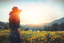 The Woman Stands On A Field Of Yellow Flowers. Sunset Atmosphere