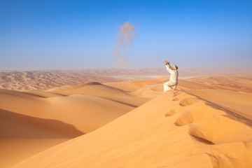 Wall Mural - arab man in tradition outfit throwing sand in the air  arabian Desert