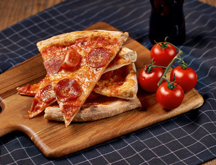 Several slices f pepperoni pizza and cherry tomatoes lying on wooden board on table