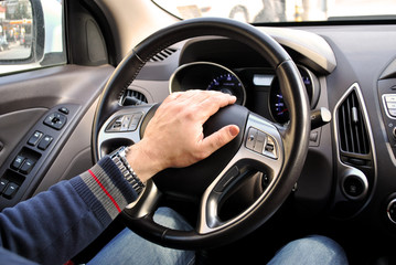 Man hand on a steering wheel in a car; man driving a car.