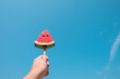 Hand holding a slice of watermelon under the blue sky with sunlight,Summer concept