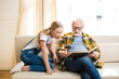 © LIGHTFIELD STUDIOS - Shocked little girl with grandfather in eyeglasses sitting on sofa and reading book