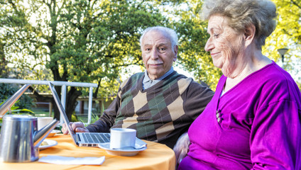 Poster - Happy elderly couple making breakfast outdoor and using laptop