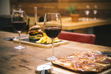 Fototapeta Uliczki - Traditional restaurant atmosphere with ham pizza and burger with chips in the background on rustic wooden table and glass of red wine