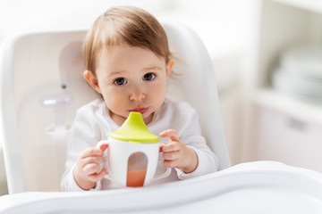 baby drinking from spout cup in highchair at home