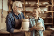 © LIGHTFIELD STUDIOS - Granddaughter and grandfather holding and examining clay goods