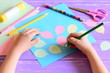 Small child doing a paper card. Child holds a pencil in hand. Card with paper air balloons, scissors, glue stick, colored paper, pencils on a table. Simple preschool and kindergarten craft projects