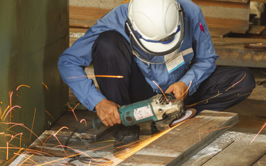 Worker with the face guard and electric wheel grinding on steel plate in factory. Heavy work concept.