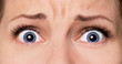 Close-up scared face of beautiful young woman with beautiful blue eyes and big pretty eyelashes and eyebrows. Macro of human eyes - surprise or shock, looking at camera.