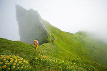 Two People Hiking By Hazy Green Mountain Side, Iceland, Europe 