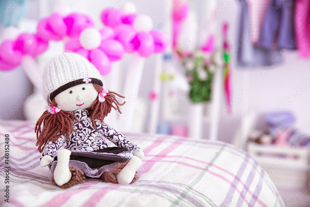 Cute doll on bed against blurred background