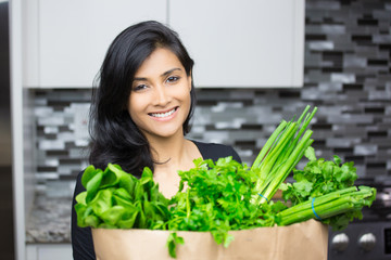 Closeup portrait, young woman with bag full of green groceries, healthy nutritious balanced diet, isolated indoors home background. Locally sourced food