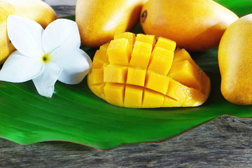 ripe mango cut in square with other yellow mangoes on a green leaf