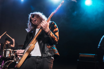 Electric guitar player with rock and roll band performing hard rock music on stage