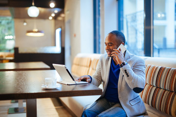 Happy young businessman sitting relaxed on sofa at hotel lobby making a phone call