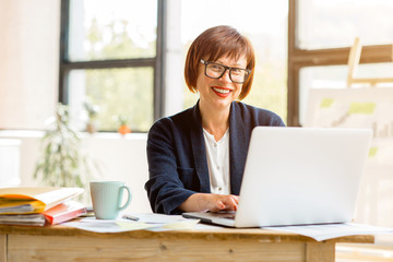 Portrait of a senior businesswoman working with documents and laptop at the bright modern office interior