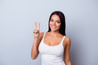 © deagreez - Peace! Portrait of a playful young latino american girl. She is in a casual white singlet standing on the pure light blue background