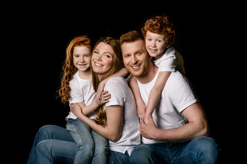 Happy redhead family sitting embracing and smiling at camera isolated on black