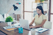 © deagreez - Smiling businesswoman is using headset when talking to customer and typing on her laptop in the nice modern work station
