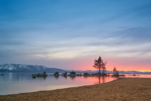 Sunset At Lake Tahoe With Sand Beach, Mountains Covered By Snow At Background