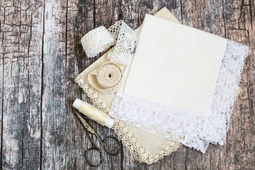  Needlework. Two handkerchiefs with decorative trim, lace, a reel of sewing threads and scissors on an old wooden background.