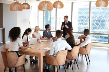 Businessman Stands To Address Meeting Around Board Table