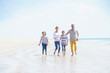 © goodluz - Happy family of four walking on sandy beach