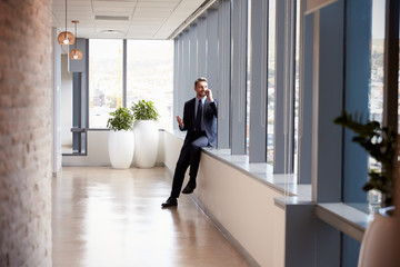 Wall Mural - Businessman Making Phone Call Standing By Office Window