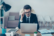 © deagreez - Young handsome serious smart freelancer in suit and spectacles sitting at office and working with laptop
