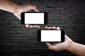 Two hands holding horizontal the black smartphone with blank screen, old brick wall background.