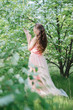 Beautiful young girl in a delicate tulle dress stands among the flowering spring trees in an outdoor park. Fine art